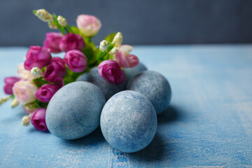 Fototapeta na wymiar Painted Easter eggs on blue background with purple flowers. Spring holiday, symbolic food. Close up shot, copy space.