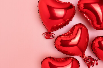 Red inflatable foil balloons in a heart shape. Festive concept on a pink glittering background with copy space.