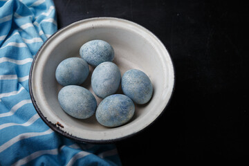 Easter eggs painted blue in white bowl on black wooden background with striped fabric. Copy space