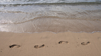Footprints at golden sand, footsteps. Blue ocean wave on sandy beach. Beach in sunset summer time. Beach landscape. Tropical seascape, calmness, tranquil relaxing sunlight.