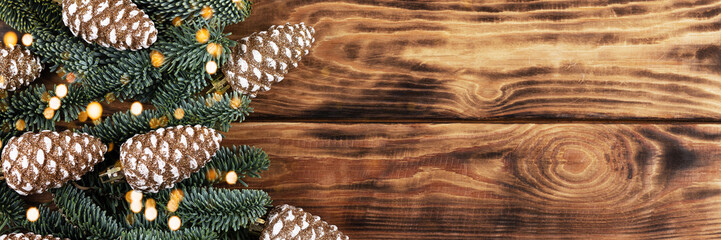 Green branches of a Christmas tree with decorations in the form of golden cones on a wooden background with twinkling festive lights with a place for text. Top view, banner