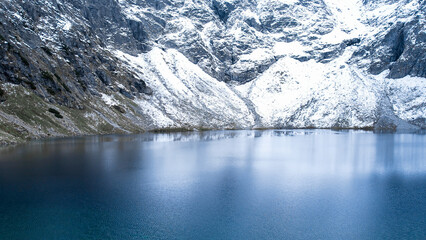 Czarny Staw pod Rysamy or Black Pond lake near the Morskie Oko Snowy Mountain Hut in Polish Tatry mountains, drone view, Zakopane, Poland. Aerial view shot of mountains in dark clouds and reflection © anna.stasiia
