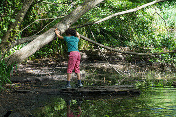 Naklejka na ściany i meble London, England - An unidentified young boy balances on a log in a pond, holding on to a tree overhead. Image has copy space.