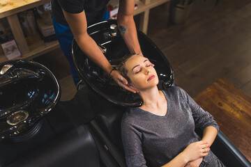 Plakat A client having her hair washed with shampoo by hairdresser in a professional hair salon. High quality photo