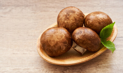brown champignon button mushroom and green leaf in wood bowl on wooden table background. pile of brown champignon button mushroom.                                                                    