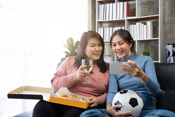 Friends watch sports on mobile phone, cheer and celebrate. Happy diverse asian friend supporters fans sit on couch with popcorn and drinks