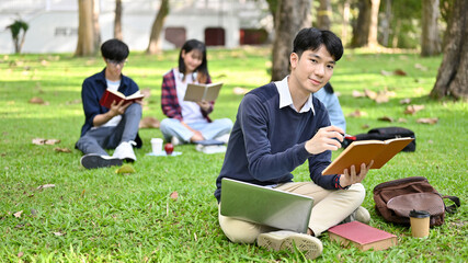 Handsome Asian male college student doing homework in the campus's park in the afternoon.