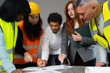 Group of five multiethnic people analyzing and studying new strategy. Architects and engineer with protective equipment.