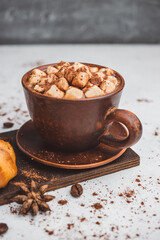 Hot chocolate drink with marshmallows in a cup and sweet bakery eclair dessert sprinkled with cocoa powder on white table