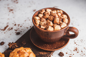 Hot chocolate drink with marshmallows in a cup and sweet bakery eclair dessert sprinkled with cocoa powder on white table