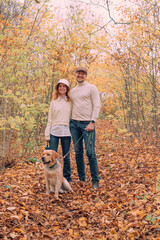 Naklejka na ściany i meble young happy cheerful couple playing with their labrador retriever dog outdoors in autumn forest. Family with a pet having fun