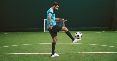 Cinematic image of a soccer freestyle player making tricks with the ball on a artificial grass court indoor. Concept about sport and people lifestyle	