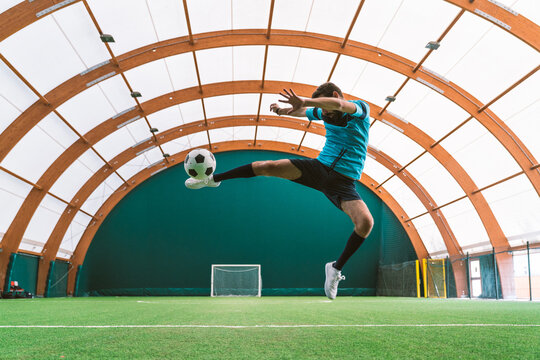 Cinematic image of a soccer freestyle player making tricks with the ball on a artificial grass court indoor. Concept about sport and people lifestyle	