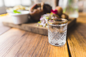 Roasted pork knuckle served in modern way on a wooden plate blurred in the background. Glass with water or vodka in the foreground. High quality photo