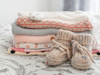 a stack of children's things, knitted shoes, cotton on a gray-white background. Knitwear, clothes made of cotton and natural materials.