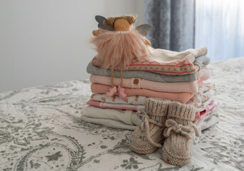 a stack of children's clothes in pink and gray tones, an angel toy and handmade knitted children's...