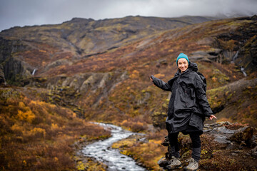 young woman with serious face points somewhere at river in mountains