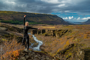youn woman in winter outwear on cliff with mountains, river and canyon at glymur waterfall in iceland
