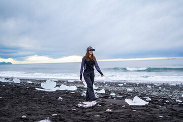 woman tourist walking on sand of black beach beetween ice  with ocean on background