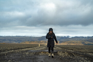 young woman walking in black winter outwear on a trail with mountains on background