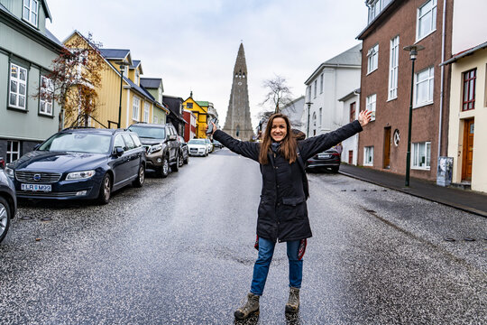young woman raising her hands in the middle of the central street of reykjavik with  Hallgrímskirkja church on background