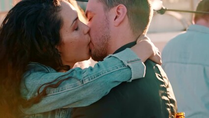 Dance, party and couple kiss, happy and smile while dancing with a crowd on a rooftop, in love and cheerful. Music, love and woman with man at festival kissing, flirt and and enjoy social event