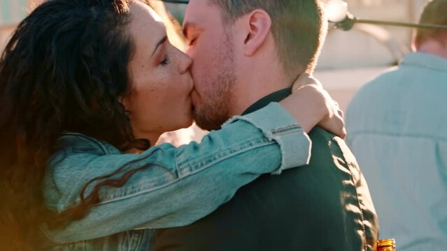 Dance, party and couple kiss, happy and smile while dancing with a crowd on a rooftop, in love and cheerful. Music, love and woman with man at festival kissing, flirt and and enjoy social event