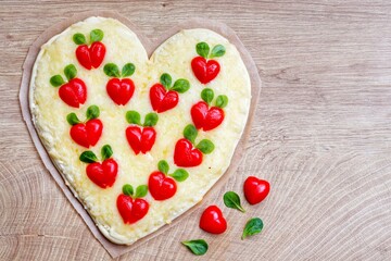 Heart shaped pizza with heart shaped tomatoes on parchment paper with wooden background.Creative art food idea for celebrate Valentine or Mother day.Top view.Copy space