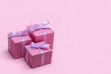 Three stylish gift boxes wrapped in pink paper, decorated with satin ribbon and bows. Pink background, copy space.