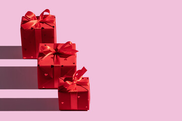 Gifts in red paper boxes with hearts, decorated with ribbon. Concept for greeting card, frame, banner. Studio shot, long shadows, copy space, pink background.