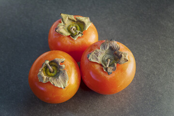 Ripe juicy persimmon fruits on a dark gray background close-up. Vegetables. Vegetarianism.