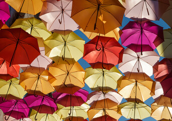 Backlit colorful umbrellas hanging from the sky decorating a street.