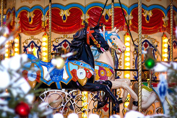 light and black horses on the merry-go-round in winter at the Christmas market