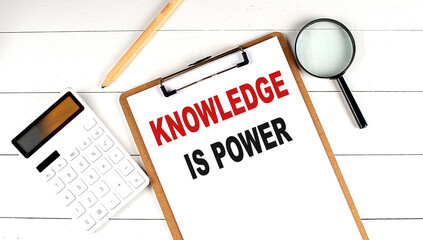 KNOWLEDGE IS POWER words on clipboard, with calculator, magnifier and pencil on the white wooden background