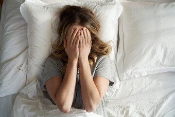 From above caucasian woman lying in the bed and covering face in hands