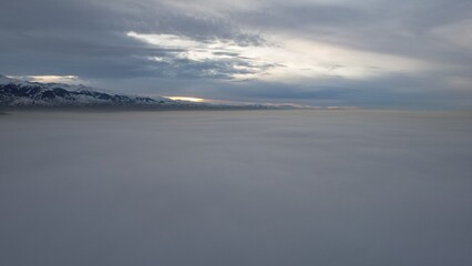 Flying a drone among the clouds with a view of the mountains. The light yellow rays of the sun at sunset are reflected on the surface of the clouds. Double layer of clouds. Mountains are visible