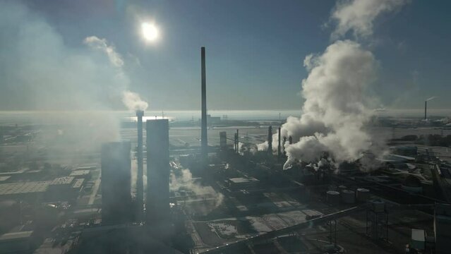 Smoke and steam rising of an industrial facility, CO2 emissions, air pollution, exhaust gases, frosty backlit scene, aerial drone shot