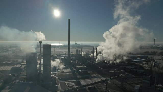 Smoke and steam rising of an industrial facility, CO2 emissions, air pollution, exhaust gases, aerial drone shot, backlit scene, moving sideways