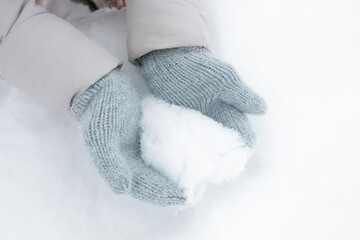 Close-up hands in wool handmade knitted grey warm mittens make heart from white snow on frost...