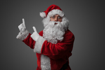 Portrait of old santa claus dressed in red suit pointing up.
