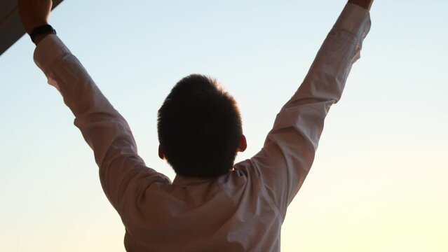 A man raises his hands up in joy celebrating victory at sunset