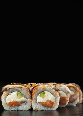 Roll made of fresh raw salmon, smoked eel, cream cheese and avocado inside on black background with reflection. Topped with Smoked Eel