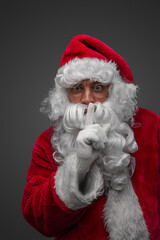 Shot of isolated on grey santa claus posing with finger at his lips.