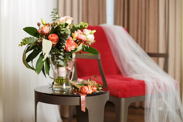 The bride's wedding bouquet and boutonniere, veil on a red chair.