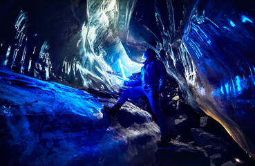 Man with blue light exploring an amazing glacial ice cave