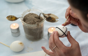 Female hands paint a white Easter egg according to Sorbian tradition with a needle head and melted candle wax
