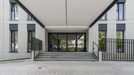 Wejście do obiektu biurowego. Elewacja wykonana z tynku i akcentami betonu. Harmonijny i spójny układ okien.