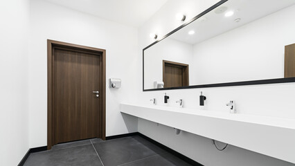 Nowoczesna toaleta z dużym oświetlonym lustrem. Szeroka umywalka z kranami na kilka osób. Jasna i przestronna łazienka. - obrazy, fototapety, plakaty
