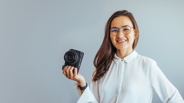Portrait of a happy photographer holding a camera and smiling at the office - creative occupation concepts. Young photographer checking photos on a camera. Photographer working in a studio