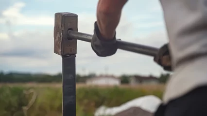 Tuinposter Sledgehammer hammering steel stake in ground. Driving a metal pile © Maksim